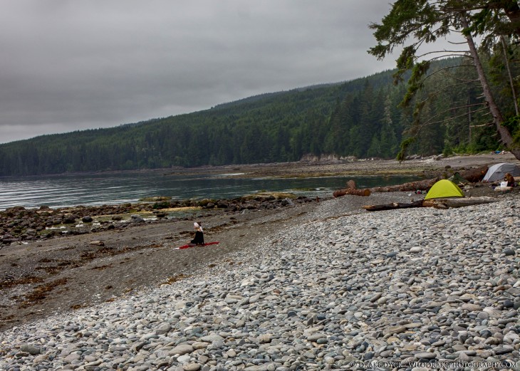 a hiker meditates on the beach near some tents