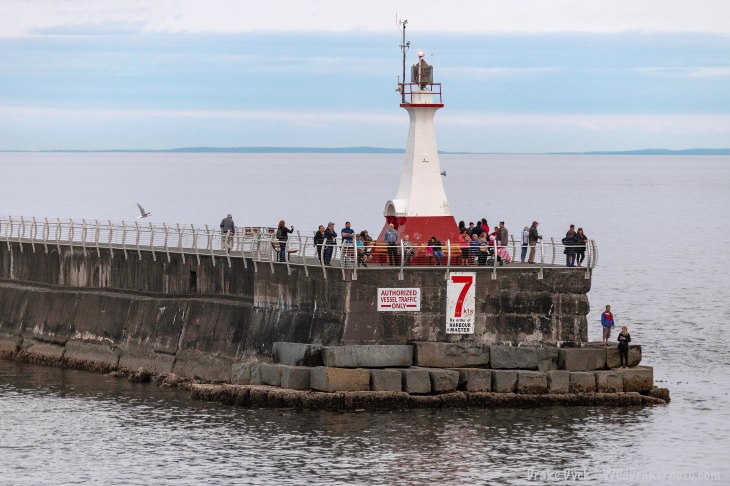 a small lighthouse on the breakwater surrounded by people